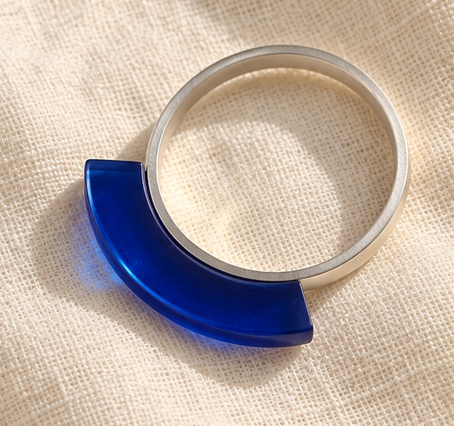 Two silver-toned open hoop earrings displayed side by side on a textured beige fabric background. The left earring features a smooth, semi-circular blue accent, while the right earring has two small, glossy blue beads at the end.